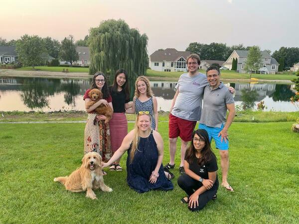 All lab members in Summer 2021 standing in front of lake, smiling and posing for picture with two cute dogs.