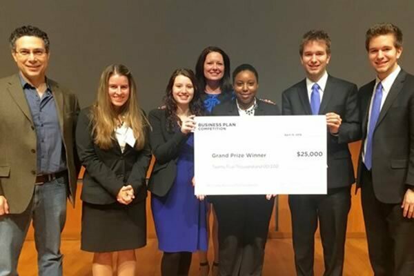 Smiling lab members in suits holding check from winning recent business competition.